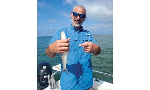 Middle-aged man wearing a short sleeve vented fishing shirt proudly displaying a fish on a boat in open waters.