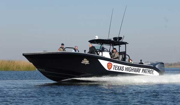 Black Texas Highway Patrol powerboat moving across the water with several male passengers 