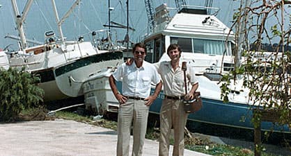 Two men posing in front of collided boats